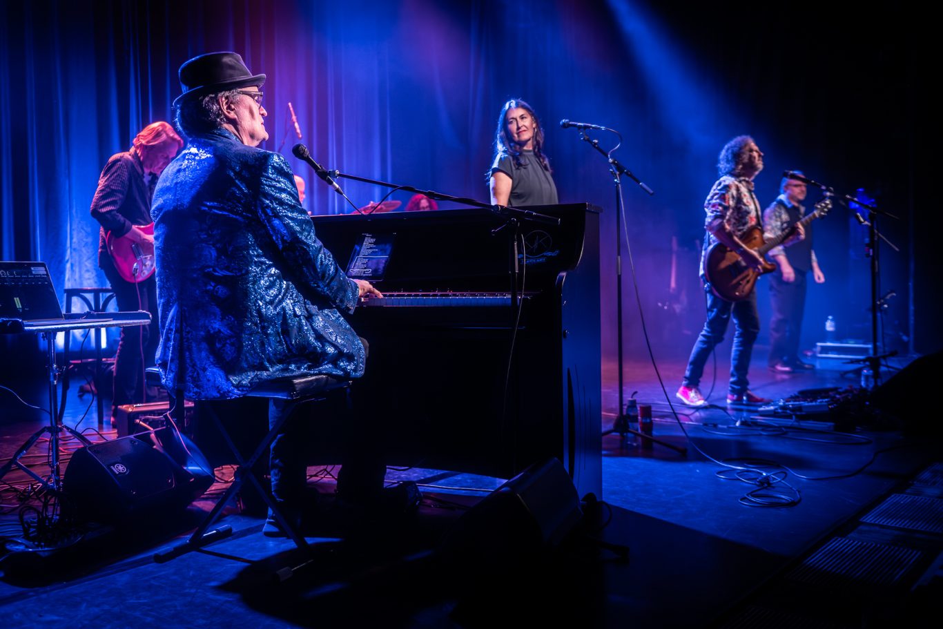 Band tritt auf, Musiker am Klavier, Bühnenlicht in Blau- und Lila-Tönen.