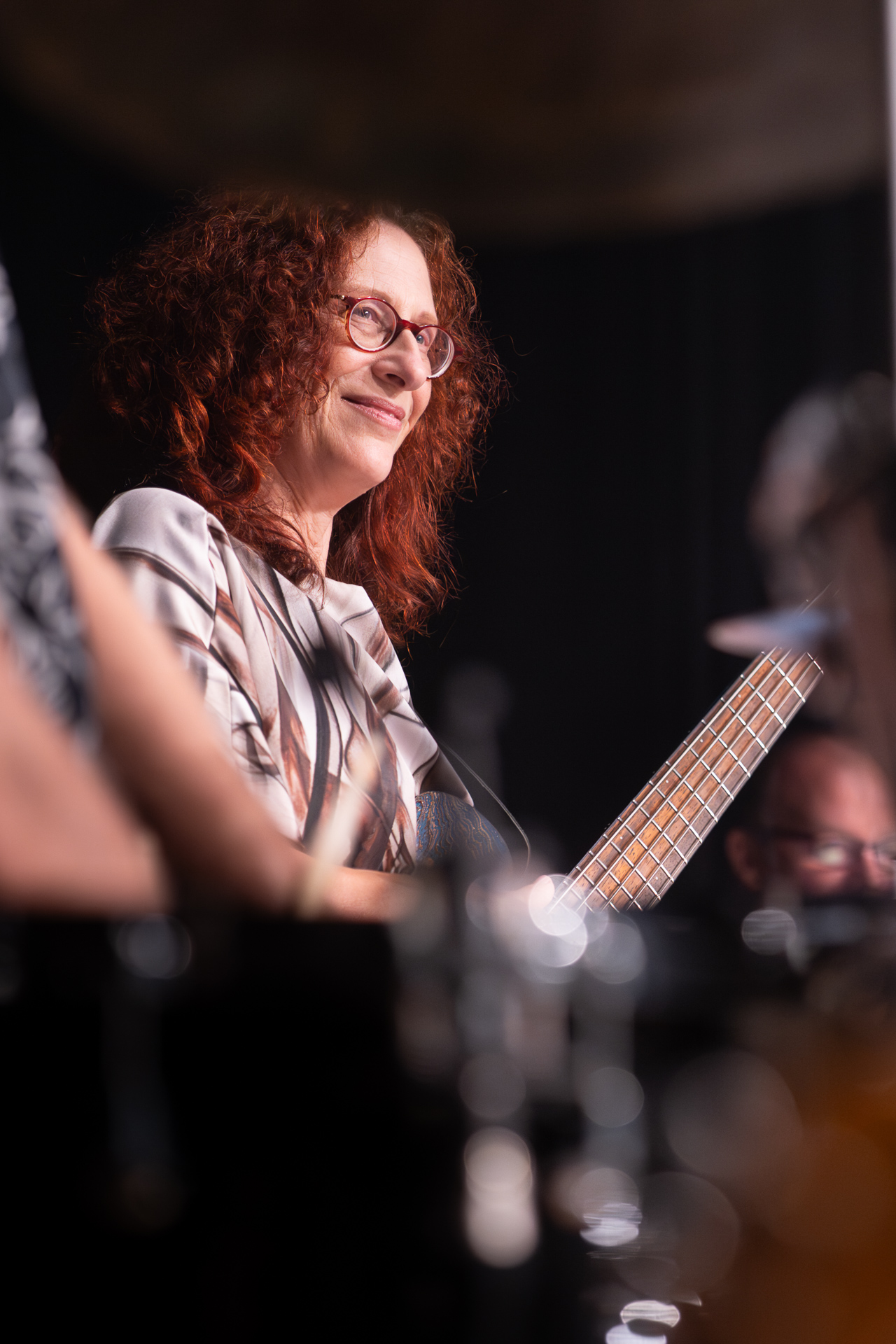 Lächelnde Musikerin mit rotem Haar, die eine Bassgitarre spielt.