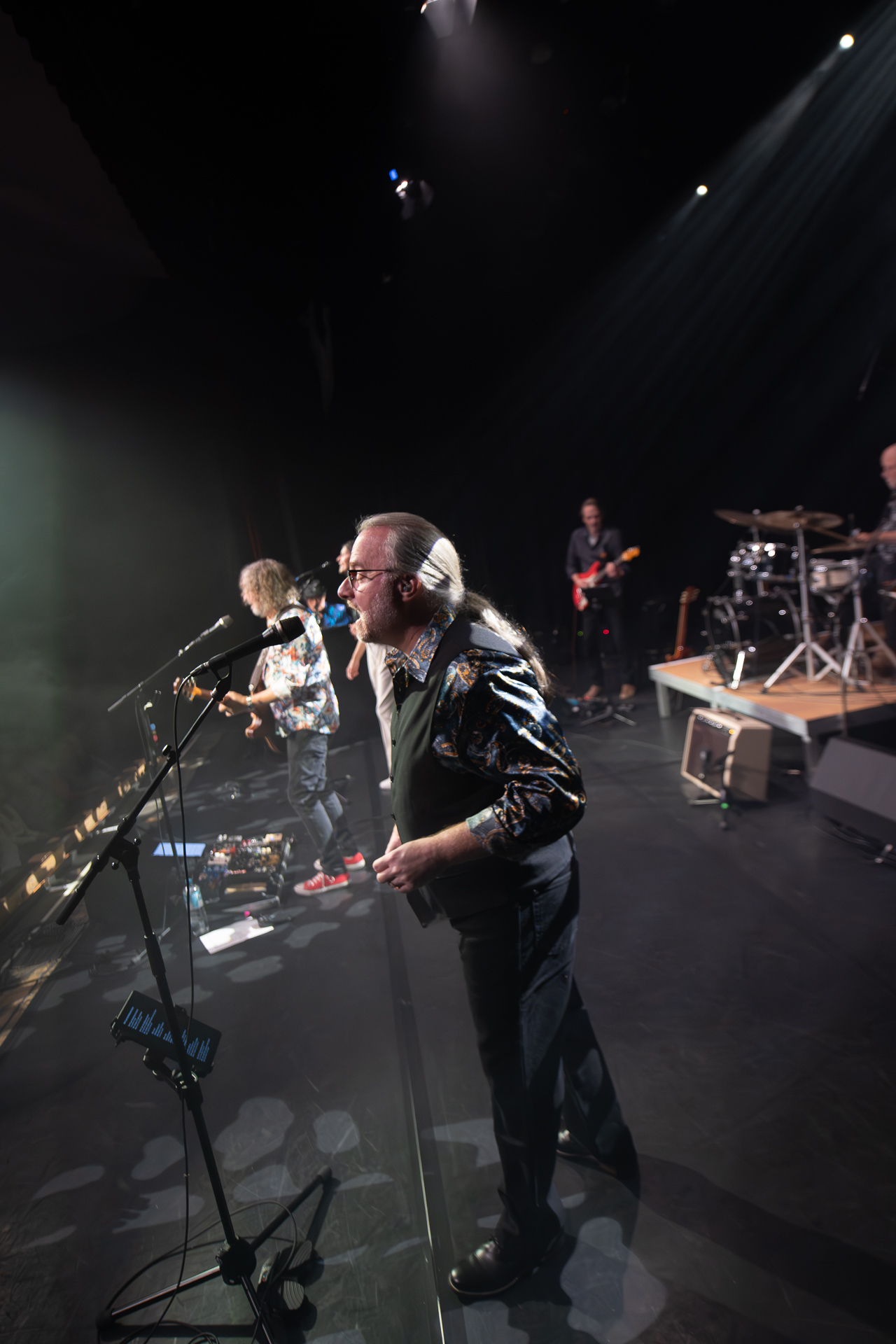 Zwei Sänger auf einer Bühne, begleitet von einer Band mit Instrumenten im Hintergrund.